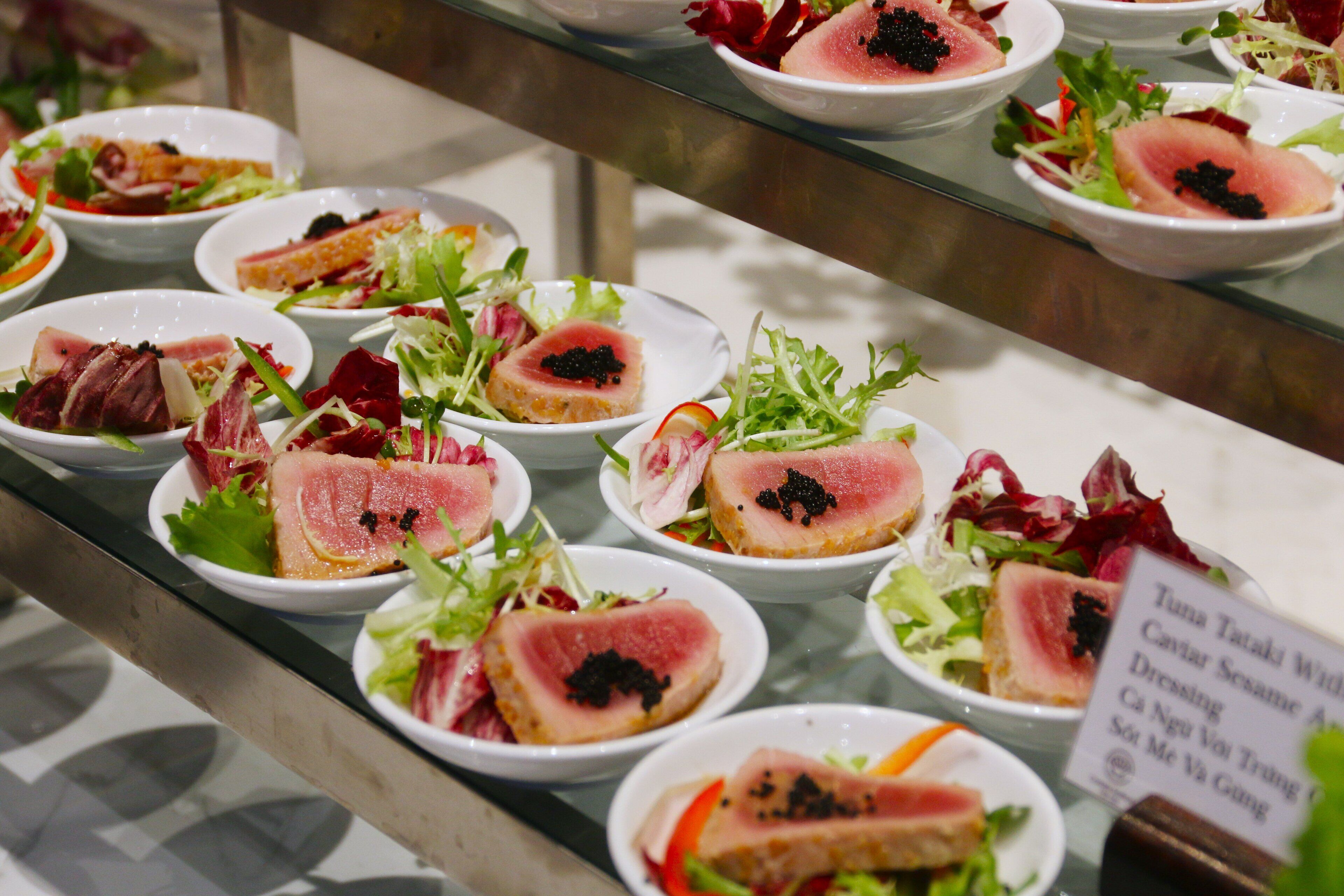 A display of various dishes, including sashimi and salads, arranged on a glass counter.