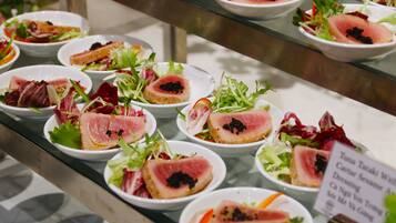 A display of various dishes, including sashimi and salads, arranged on a glass counter.