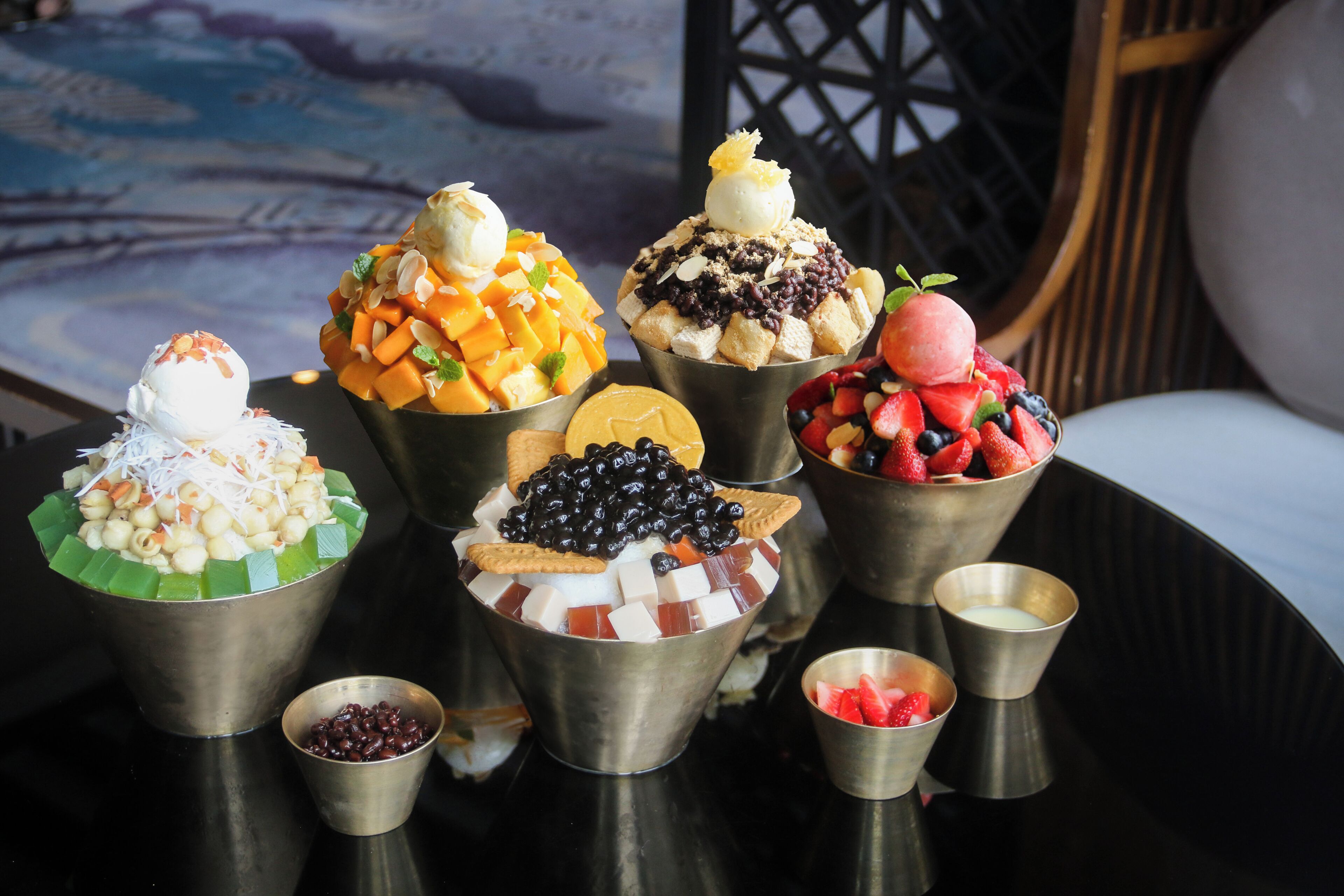 A variety of dessert bowls with different toppings and a small bowl of red beans.