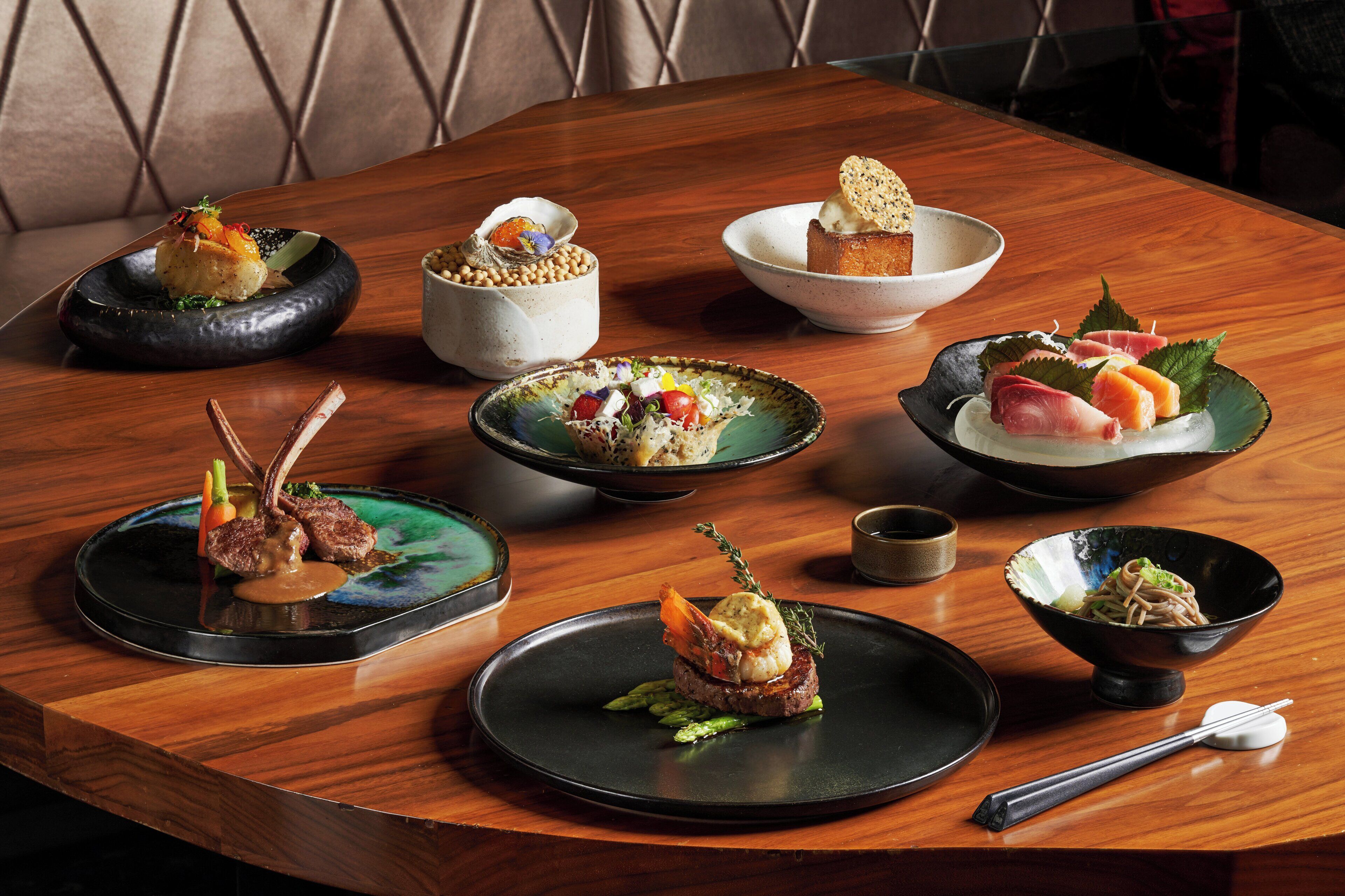 Een houten eettafel met diverse gerechten, waaronder sushi, sashimi en een toetje.