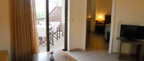 Quarto com mesa de madeira, TV em suporte e porta de vidro deslizante para área externa com varanda e deck de madeira.