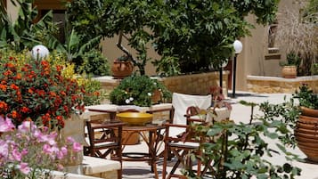 Un patio al aire libre con mesas y sillas de piedra, rodeado de macetas con plantas y flores.