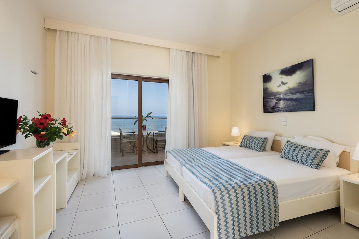 Une chambre d’hôtel comprenant un lit, une télévision, un bureau, une chaise et un balcon avec vue sur la mer.