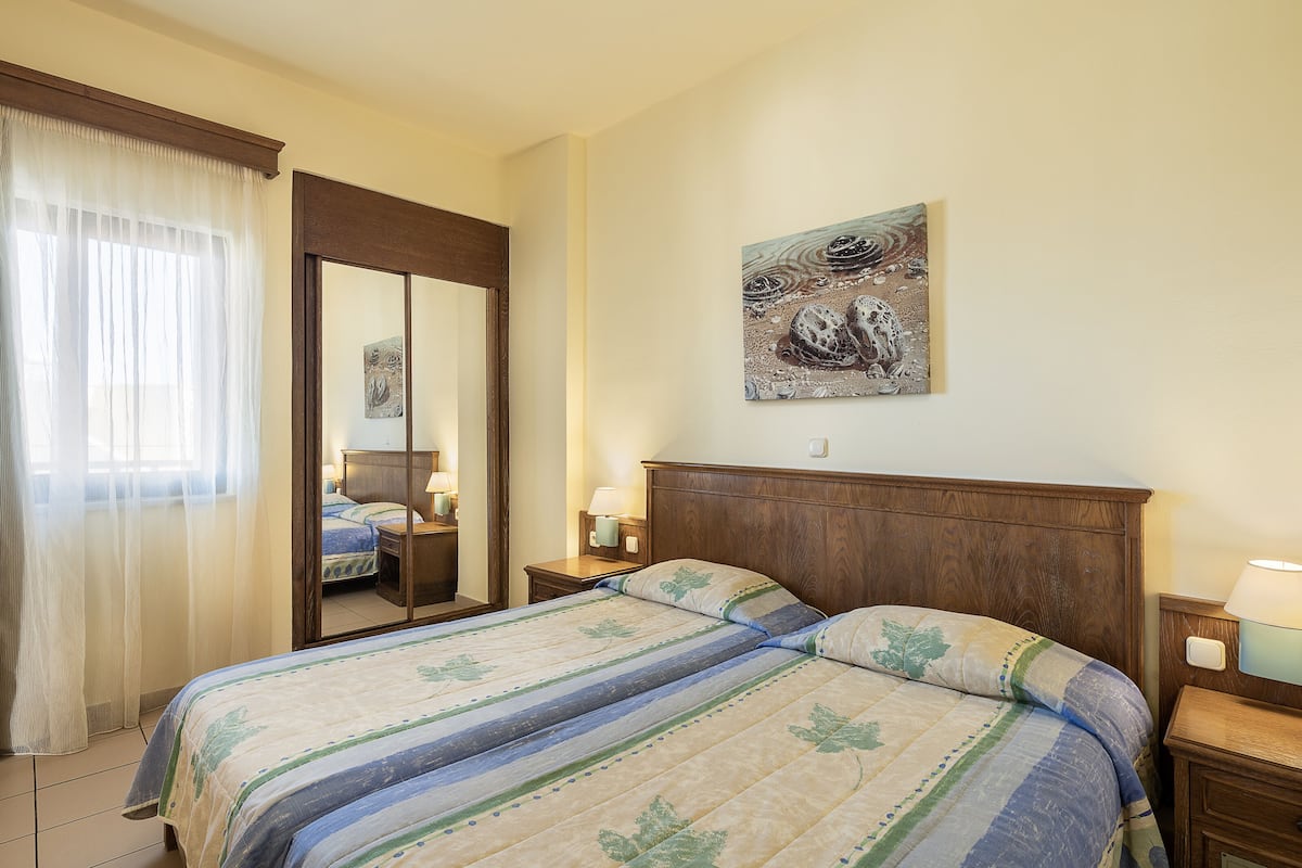 Une chambre à coucher avec un grand lit, une tête de lit en bois, une table de chevet avec une lampe, un miroir et un tableau accroché au mur.