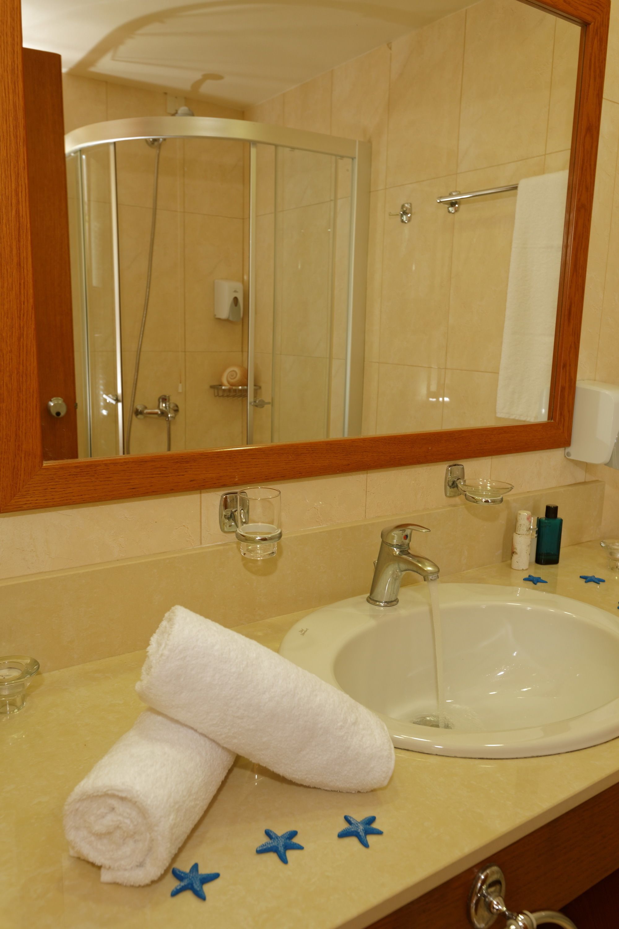 Un baño con lavamanos, espejo y ducha. Hay toallas y artículos de aseo en la encimera.