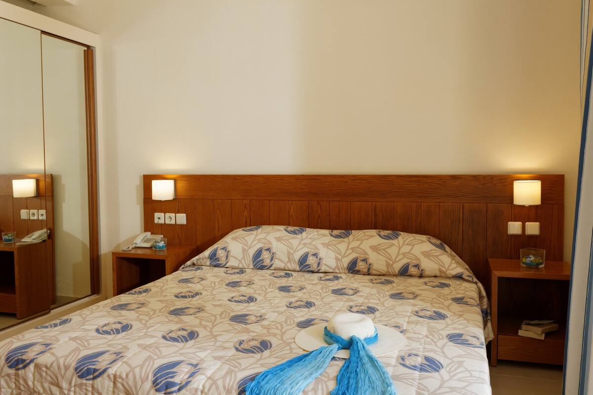 Une chambre d’hôtel avec une tête de lit en bois, deux lampes de chevet, un téléphone et une couvre-lit à motifs floraux.