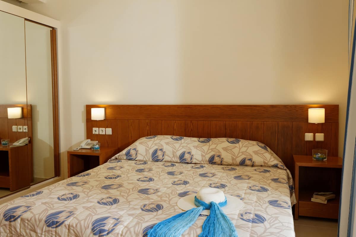 Ein Hotelzimmer mit einem hölzernen Kopfteil, zwei Nachttischlampen, einem Telefon und einer zudeckenden, floral gemusterten Bettdecke.