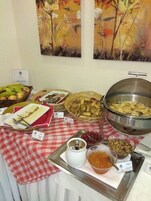 Una mesa de buffet con diversos alimentos, entre ellos frutas, quesos y un bol grande de metal.