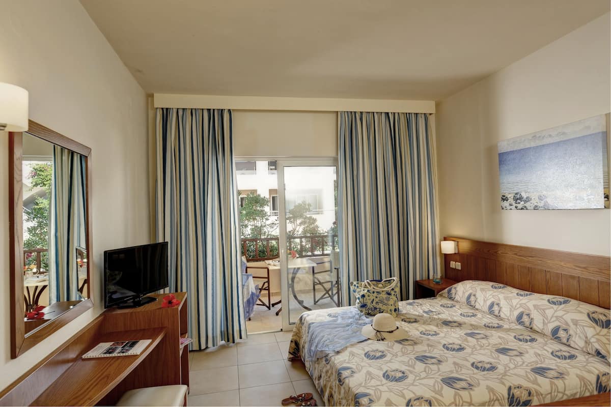 Une chambre d’hôtel avec un lit, un bureau avec une télévision, une chaise, une table et des rideaux.
