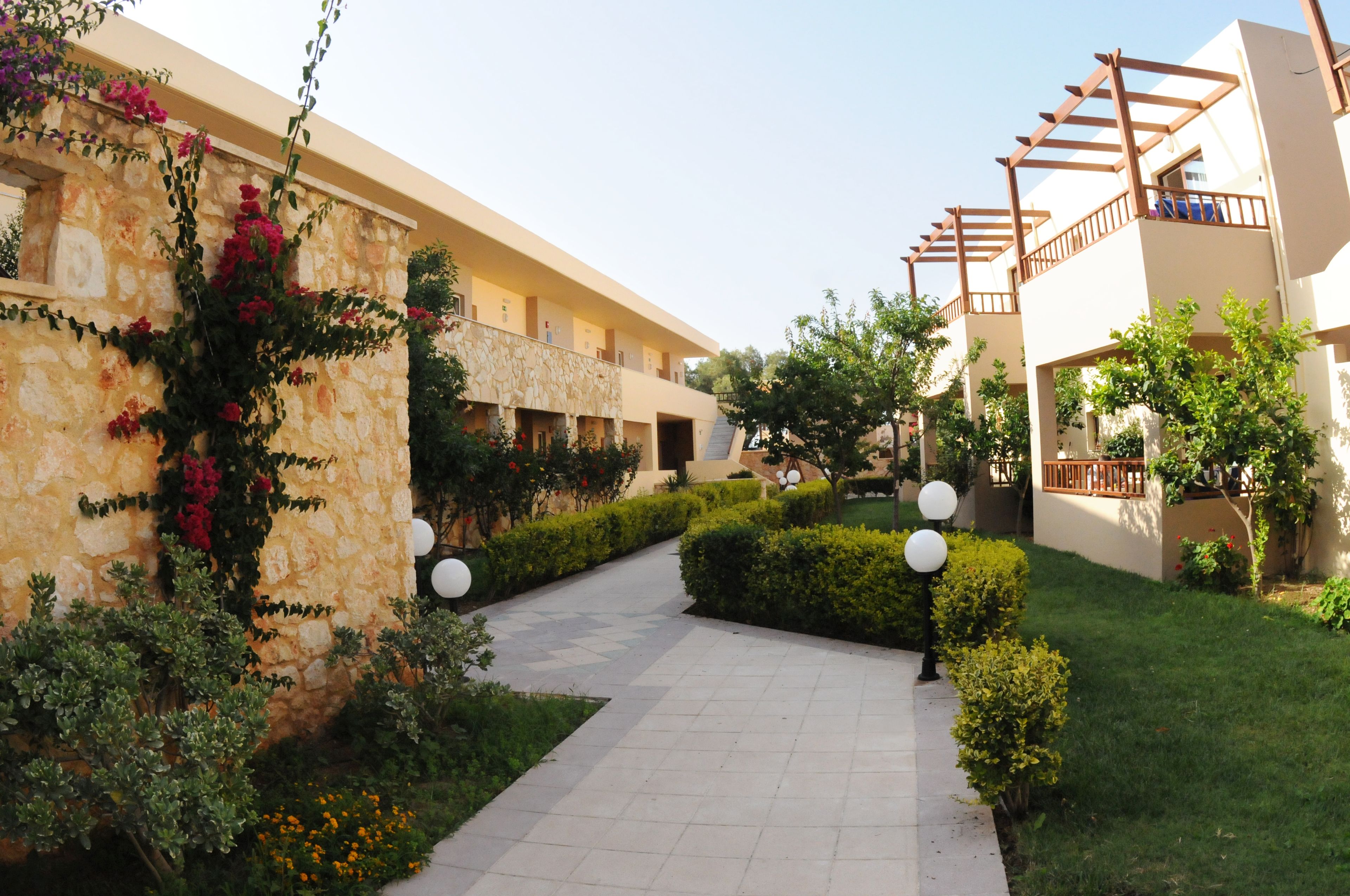 A courtyard with a pathway, stone walls, and greenery.