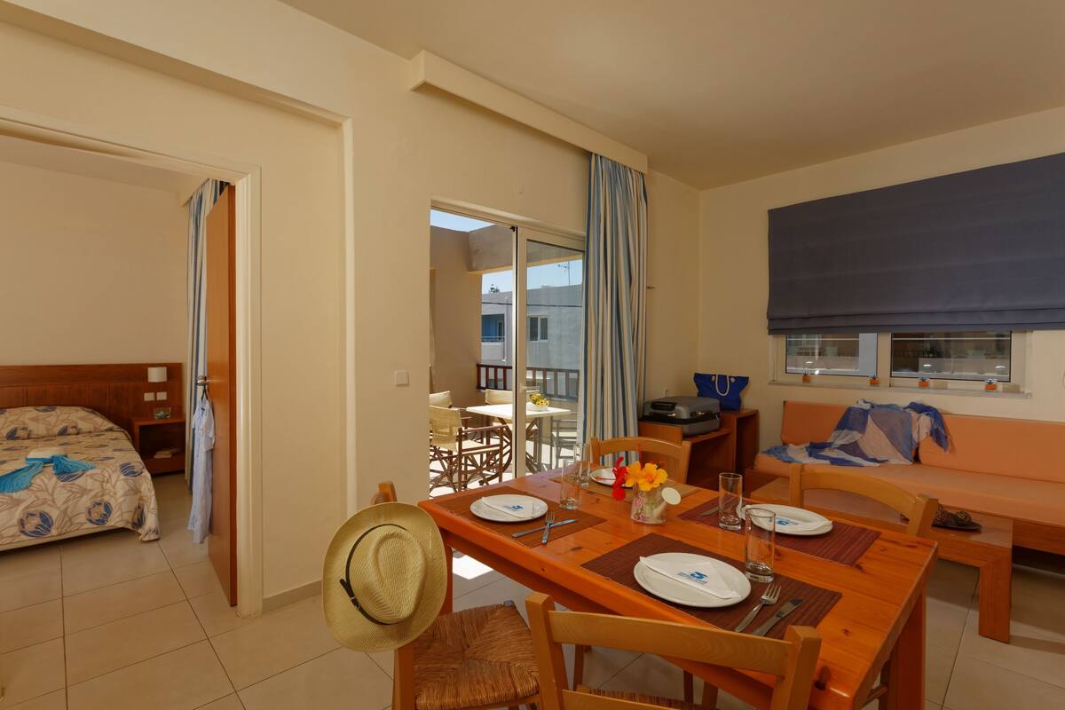 Une chambre d’hôtel avec un lit, une table à manger dressée pour deux personnes, un canapé et un balcon avec vue.