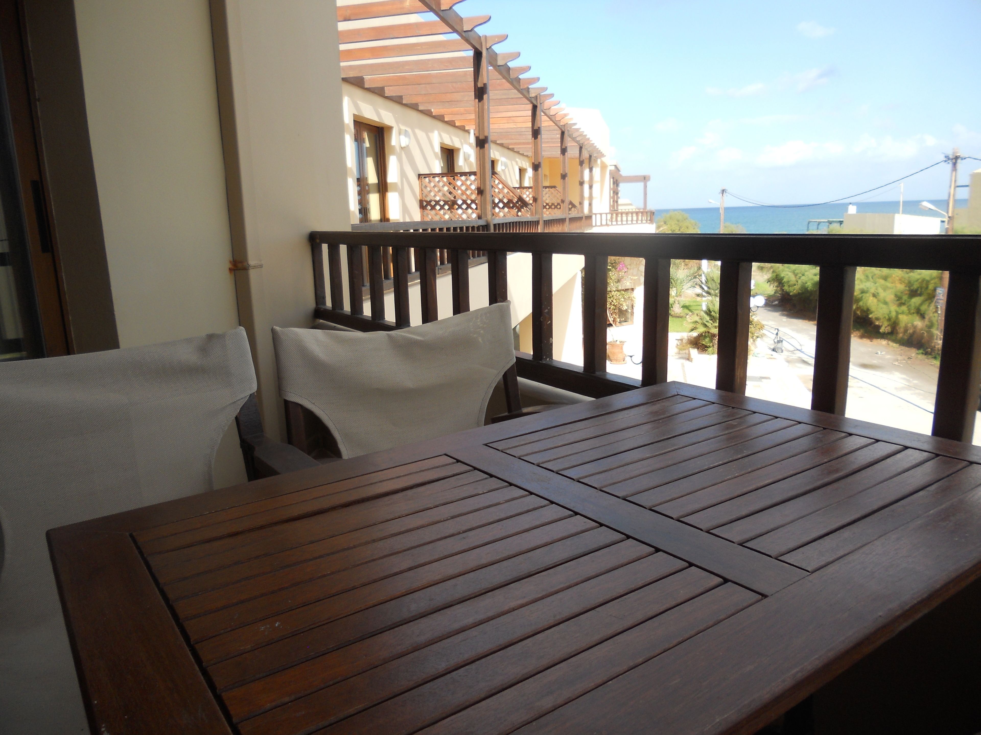 A wooden table and two chairs on a balcony with a view of the sea.