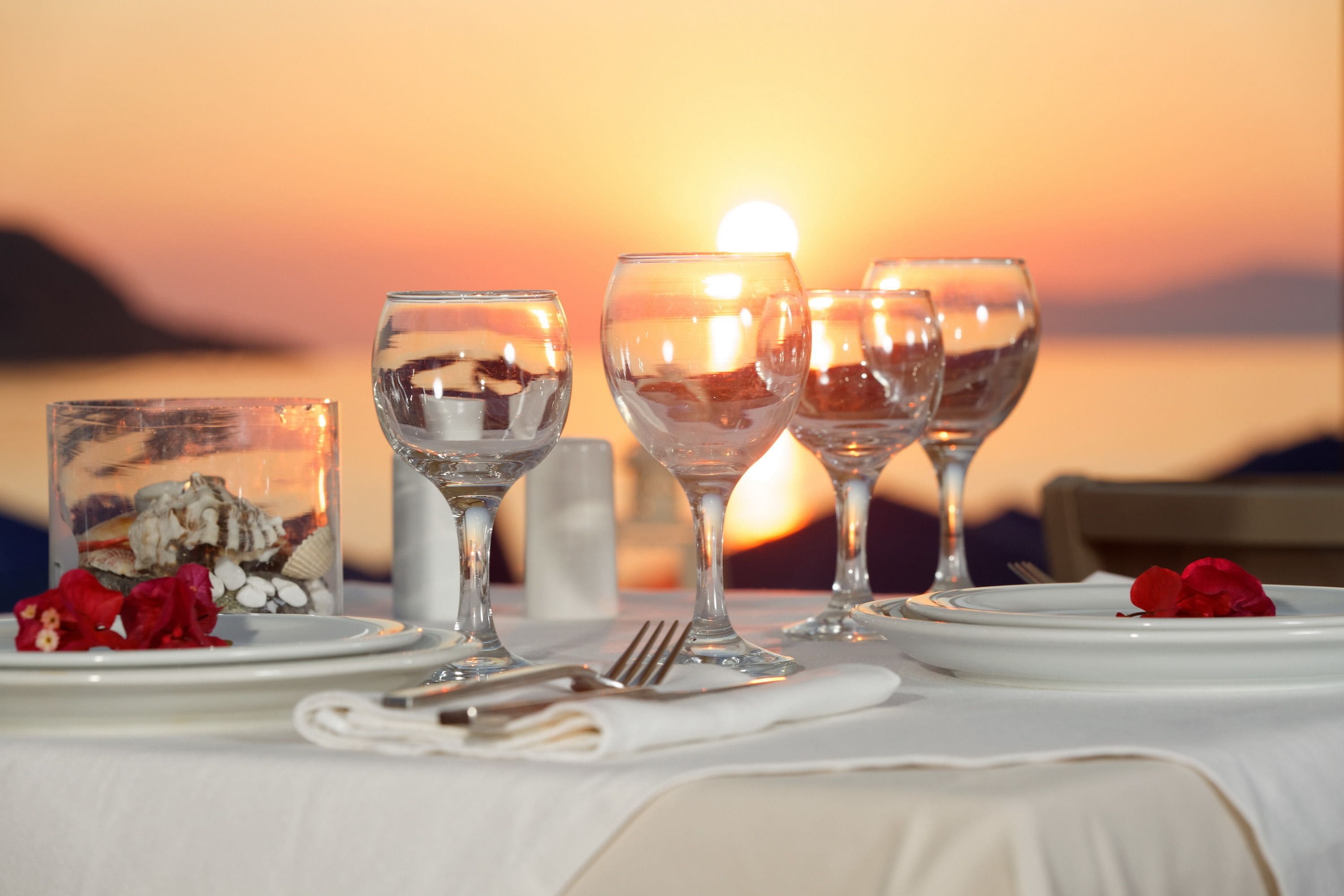 A table set for a meal with wine glasses, plates, and a candle, set against a sunset view.