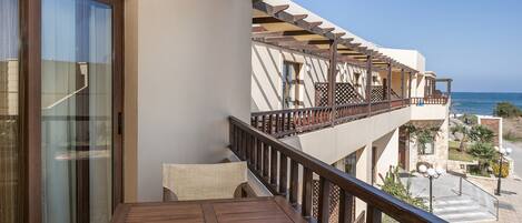 A balcony with a wooden table and chairs, overlooking a coastal view.