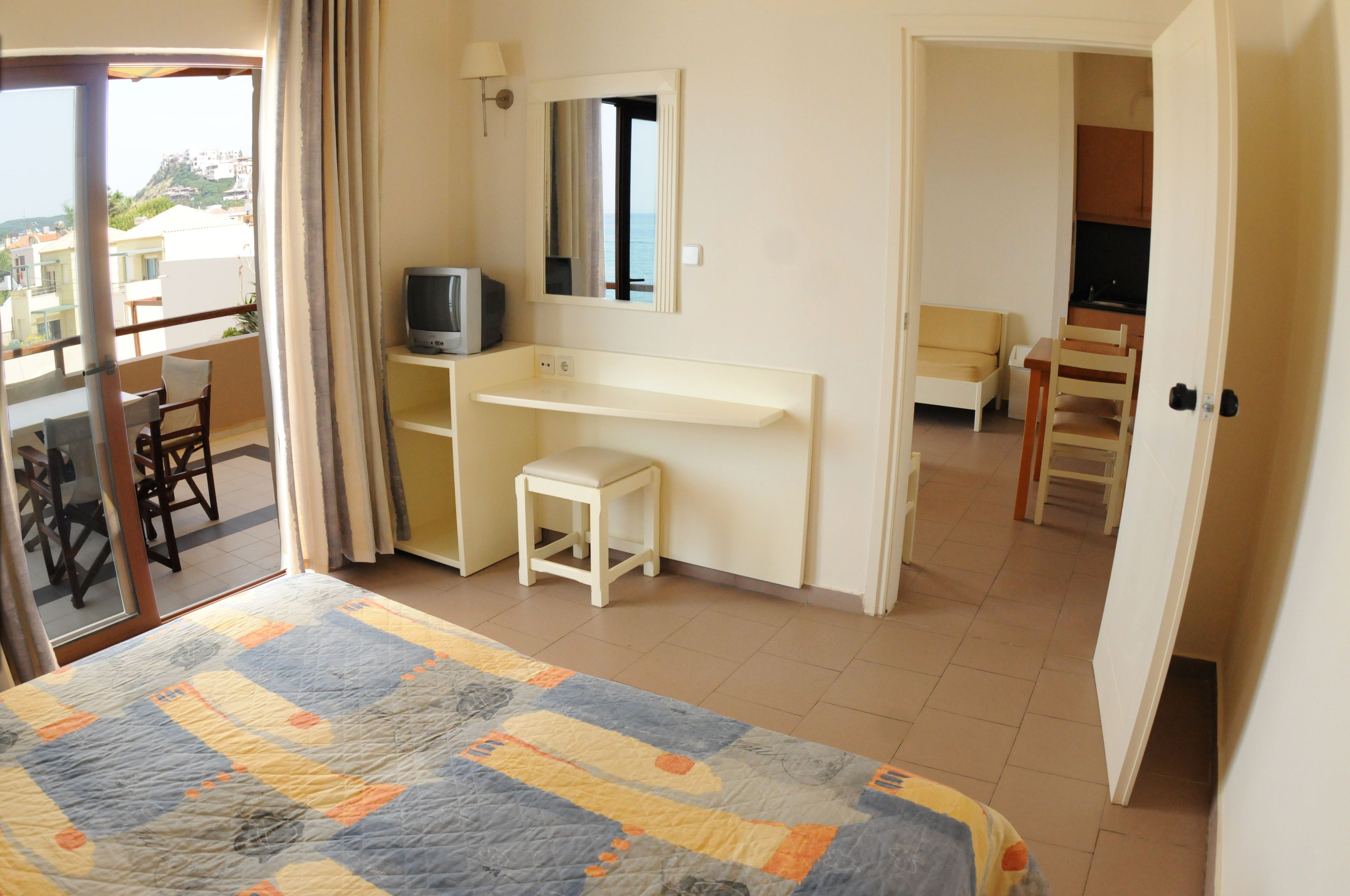 A bedroom with a bed, a desk, a chair, a television, and a view of the outside.