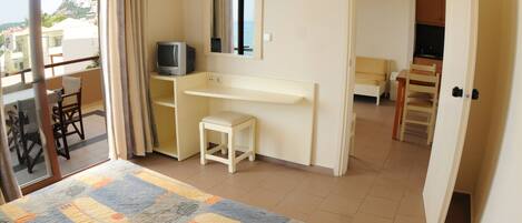 Un dormitorio con cama, escritorio, silla, televisor y vista al exterior.