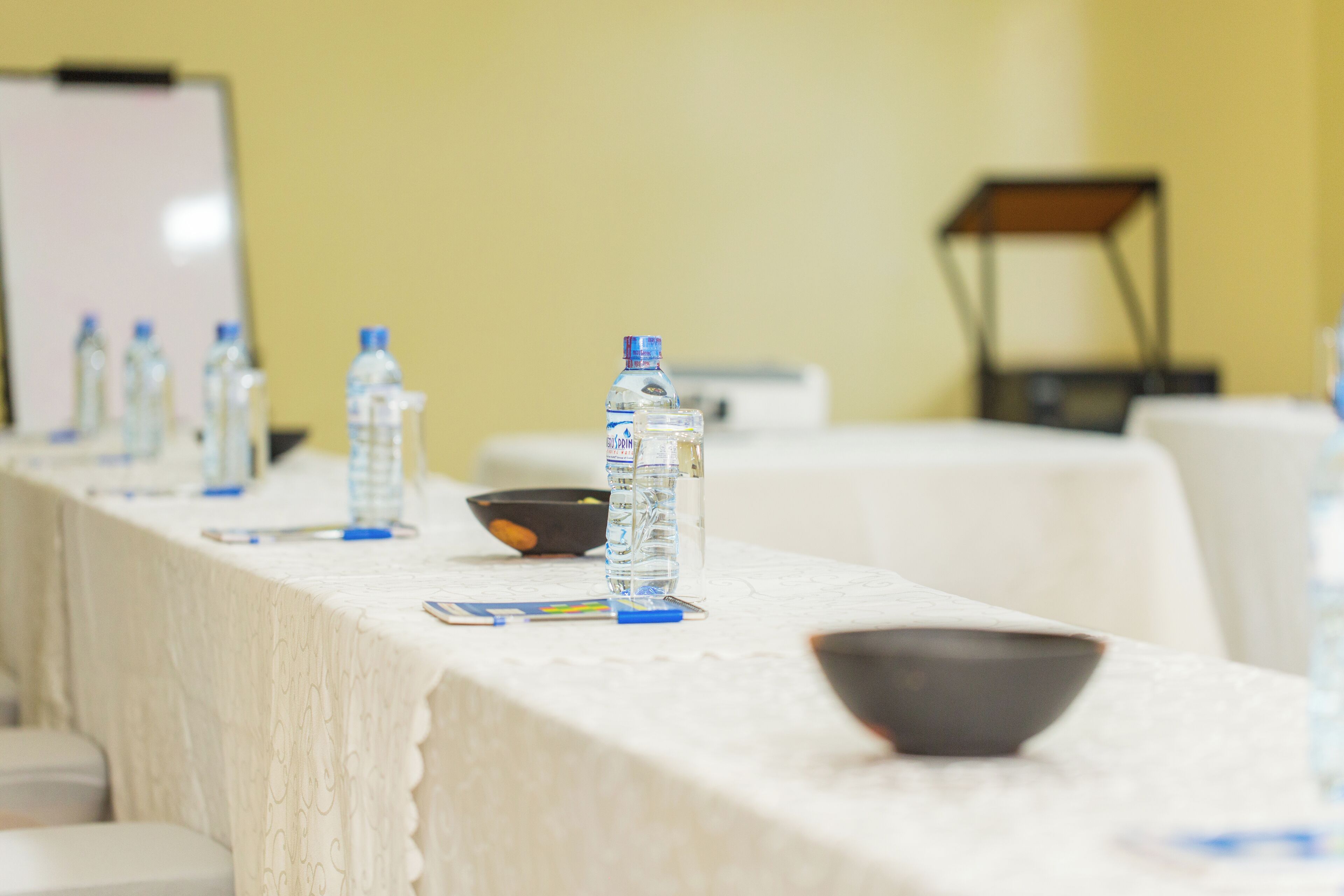 Una mesa de conferencias con botellas de agua, un bol y una pizarra de fondo.