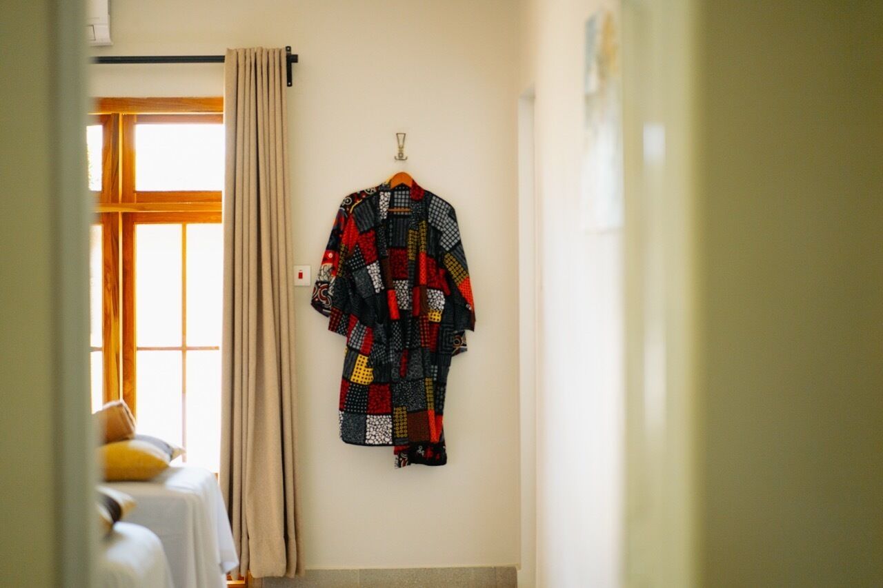 A room with a bed, a hanging quilt, and a window with curtains.