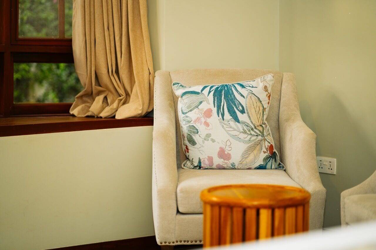 Uma poltrona bege com uma almofada floral, colocada ao lado de uma janela com cortinas bege.