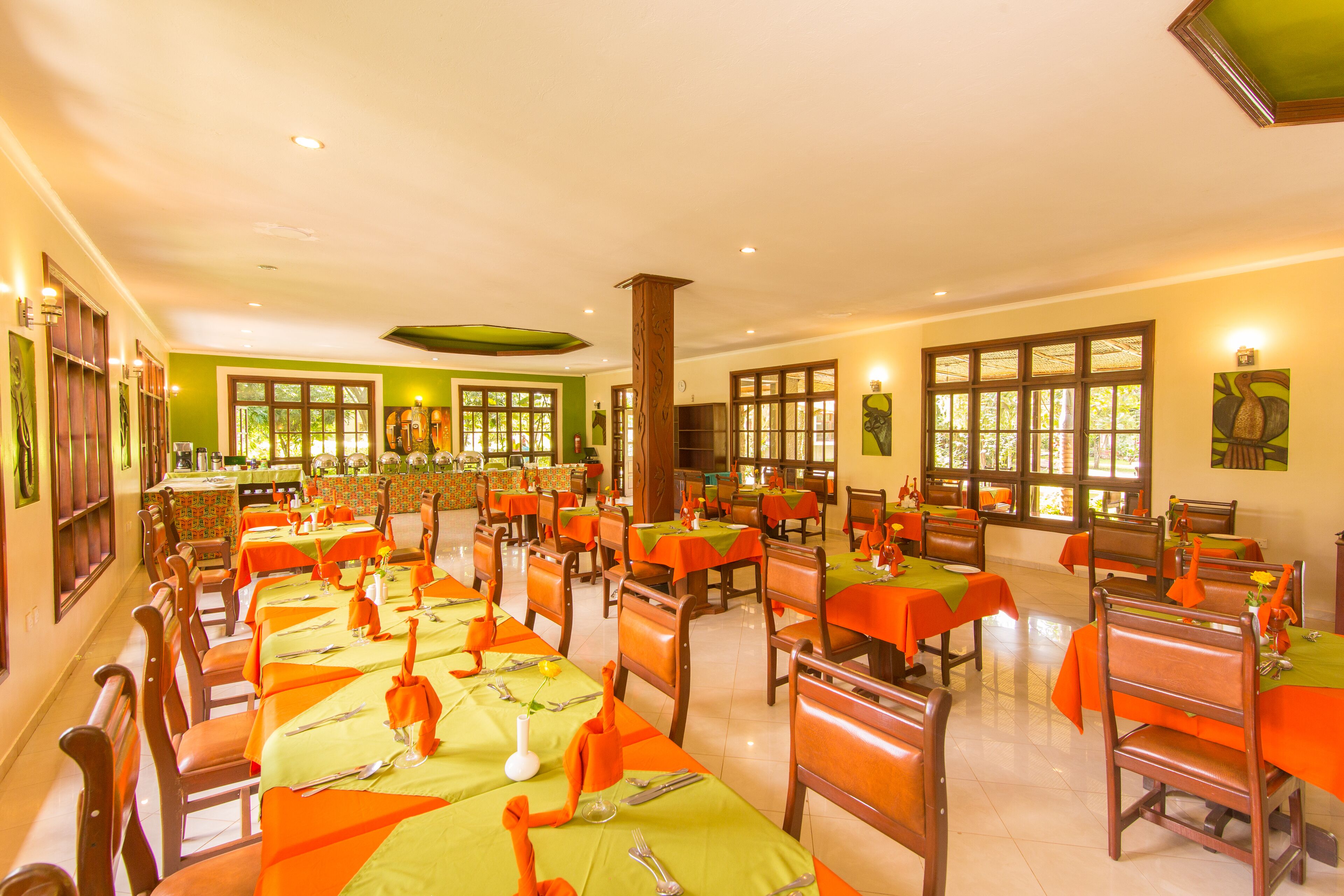 A spacious dining area with multiple tables and chairs, large windows, and a green accent wall.