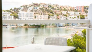 A balcony with a table and chairs overlooking a beach and a hillside of buildings. - Pierre & Vacances Mallorca Portofino (Calvia)
