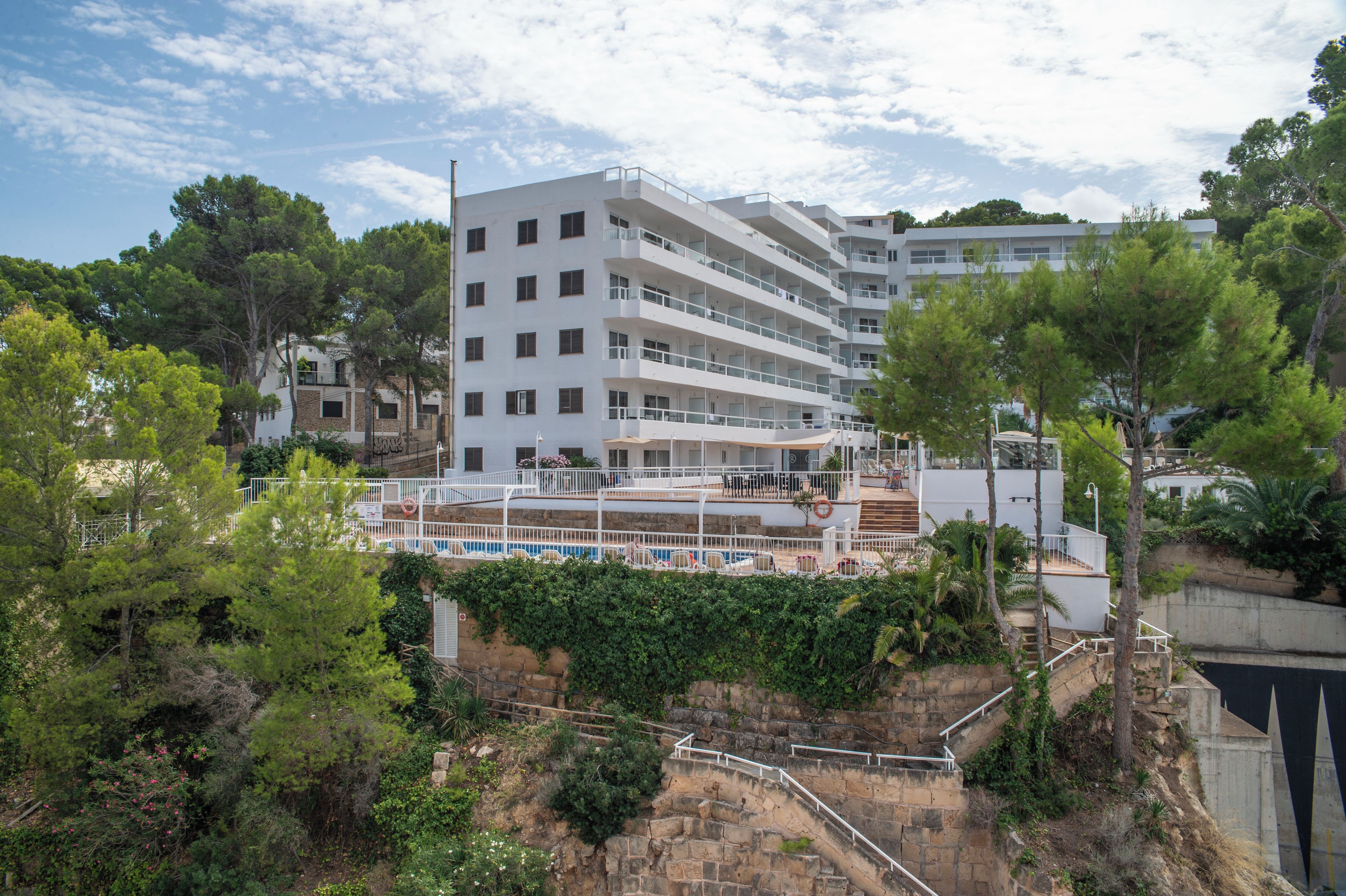 Un hotel de varios pisos con balcones, piscina y vegetación circundante.