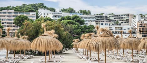 A beach with rows of sun loungers and thatched umbrellas, a clear sky, and a building with 'PORTOFINO' signage in the background.