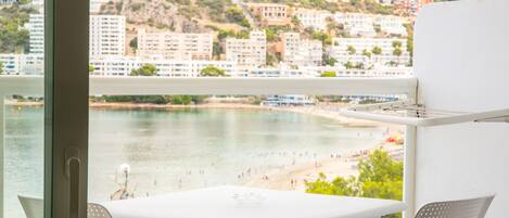 Un balcone con tavolo e sedie vista spiaggia e edifici su una collina.