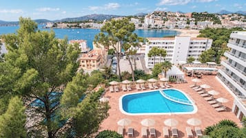 Un complexe hôtelier doté d’une piscine, de chaises longues et offrant une vue sur la mer et les montagnes.