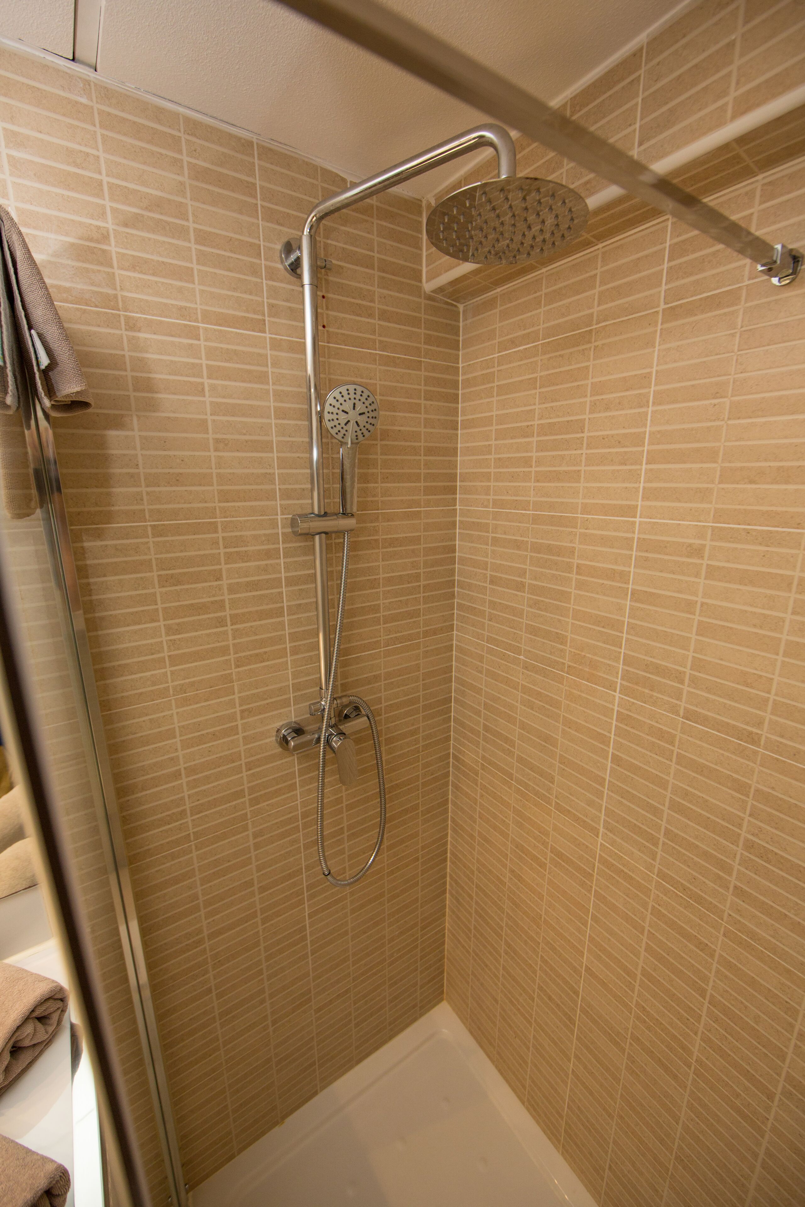 A shower with a handheld showerhead and a fixed overhead showerhead, both mounted on a wall with a tiled pattern.