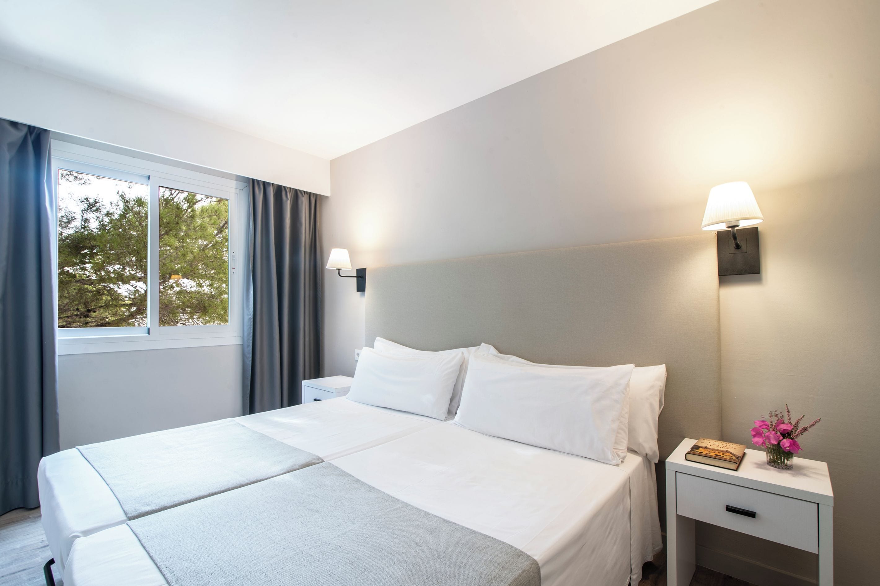 A hotel room with a large bed, a bedside table with a lamp, and a window with curtains.