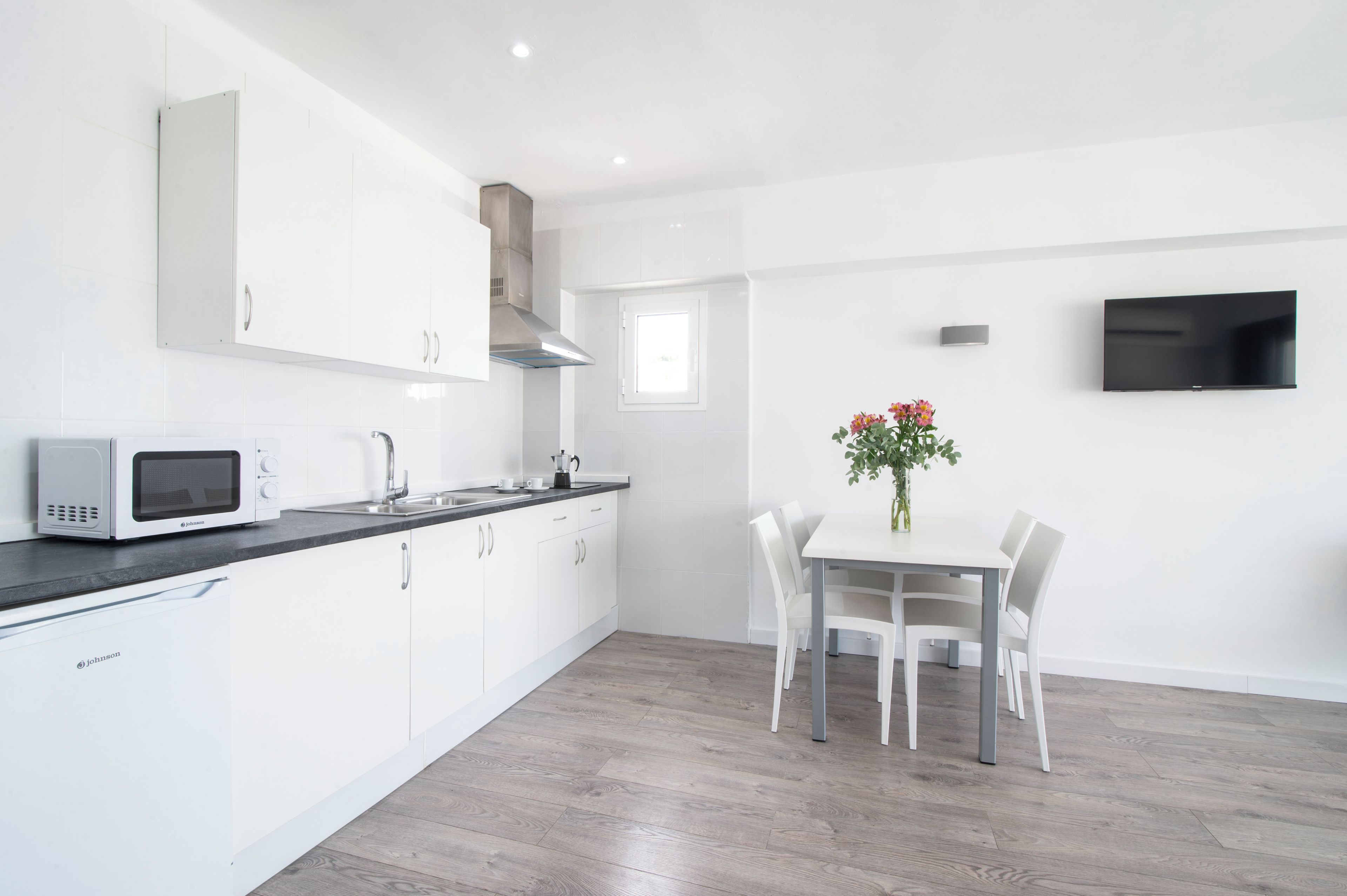 Een moderne keuken met witte kasten, een magnetron en een eethoek met een tafel en stoelen.