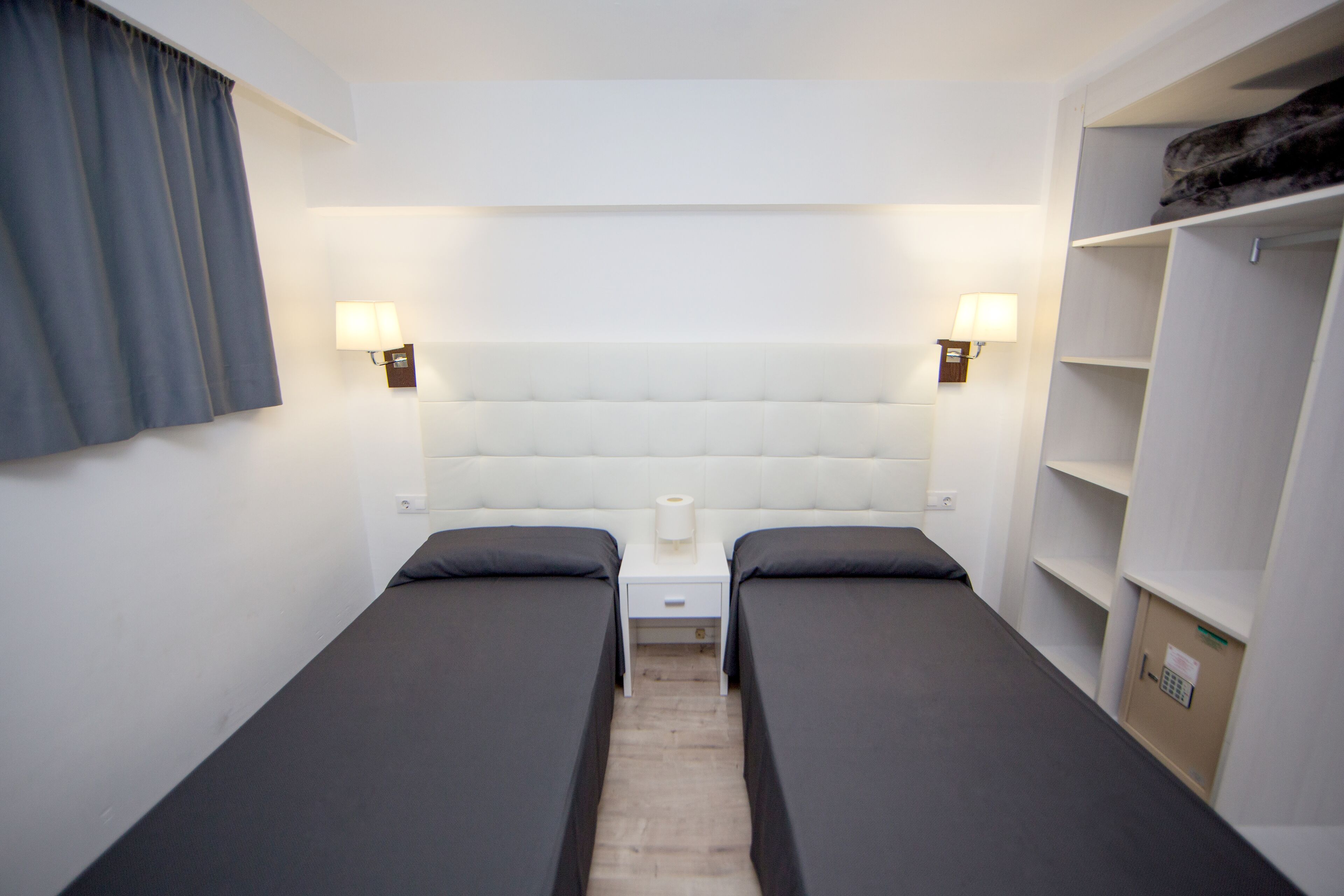 Quarto duplo com duas camas, mesa de cabeceira, abajur e guarda-roupa.