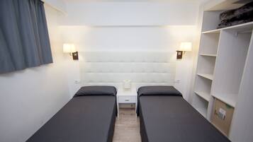 Quarto duplo com duas camas, mesa de cabeceira, abajur e guarda-roupa.