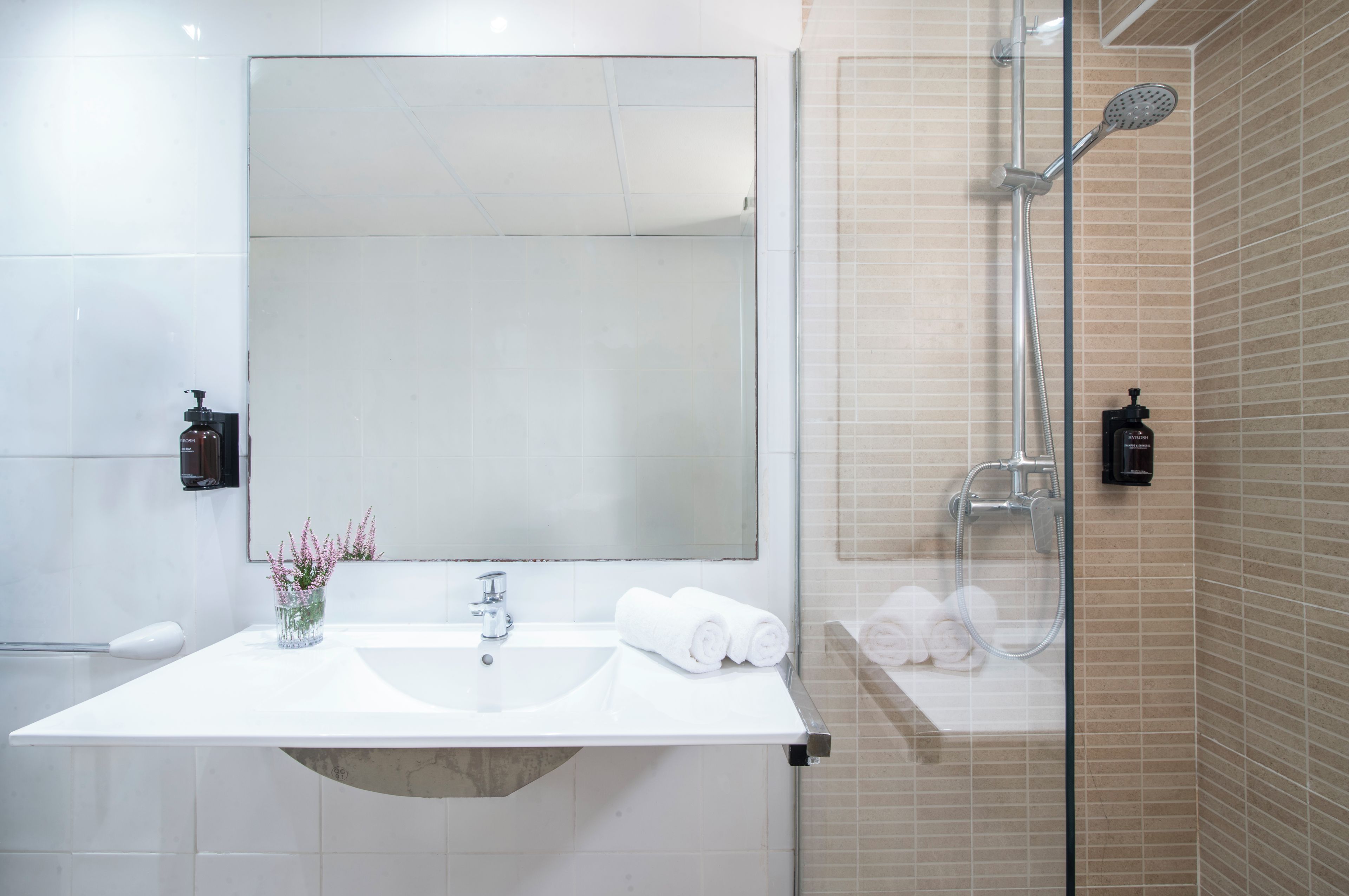A modern bathroom with a large mirror, a sink, and a shower.