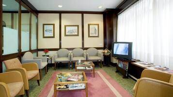 Habitación de hotel con televisión, zona de estar con sillones, una mesa de centro y cuadros en la pared.