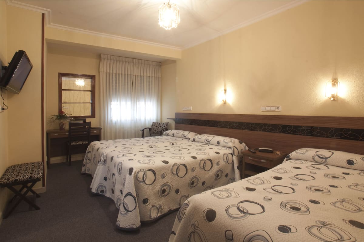 Habitació d'hotel amb dos llits, un escriptori, una cadira, un televisor i una finestra amb cortines.