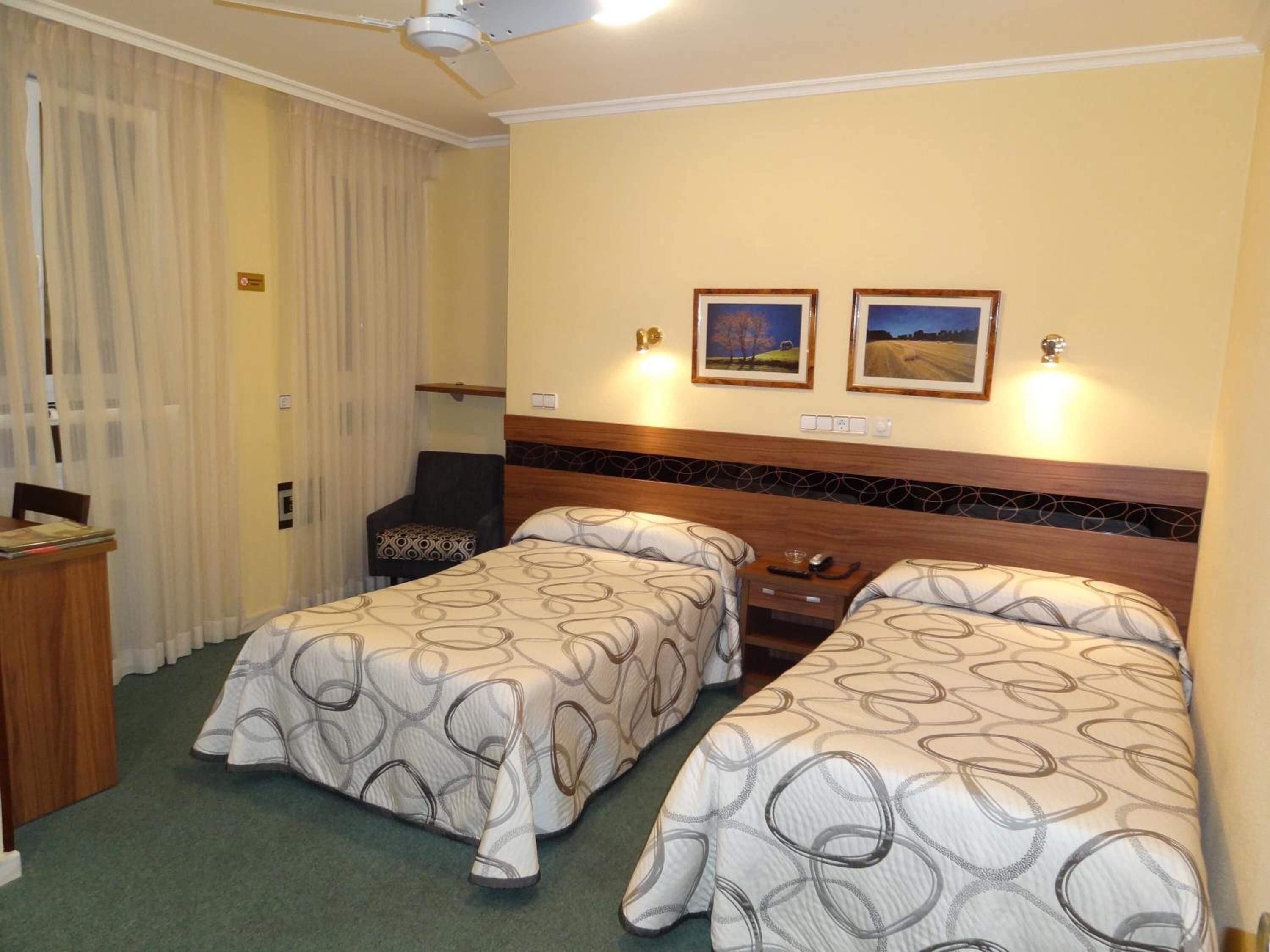 Habitación de hotel con dos camas, un escritorio, una silla y dos cuadros en la pared.