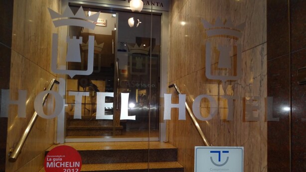 Entrada de un hotel con recepción, una escalera y carteles que indican recomendaciones de Michelin y TripAdvisor.