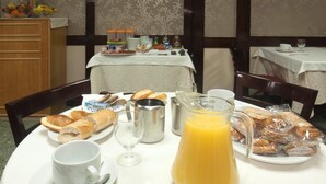 Una mesa de desayuno con pan, pasteles, una jarra de jugo de naranja y una taza de café.
