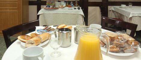 Una mesa de desayuno con pan, pasteles, una jarra de jugo de naranja y una taza de café.