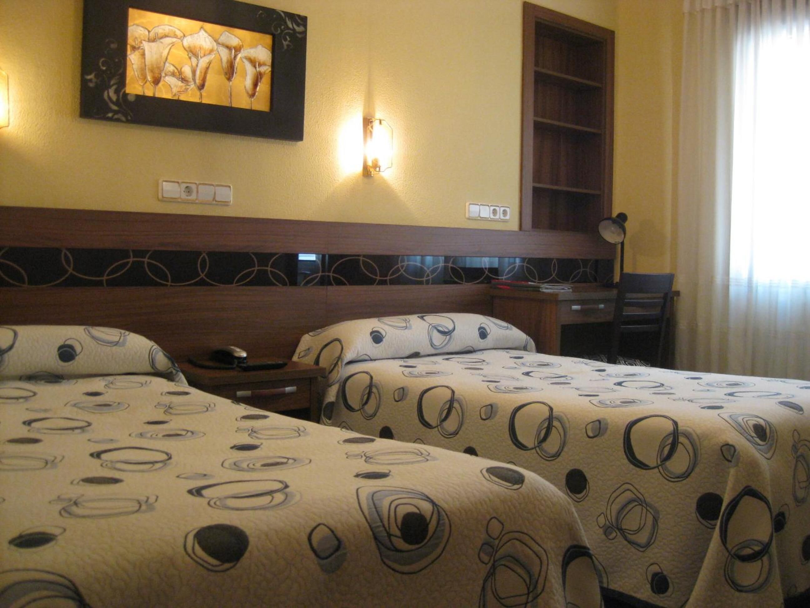 Quarto de hotel com duas camas, uma escrivaninha, uma cadeira e um quadro na parede.