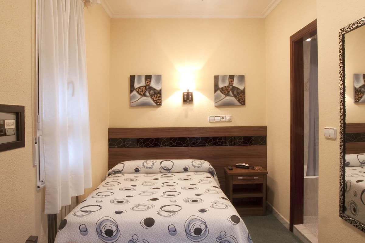 Habitació d'hotel amb un llit, una tauleta de nit, una cadira, un ventilador de sostre i obres d'art a les parets.