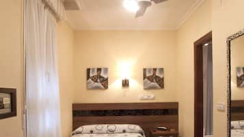 A hotel room with a bed, a nightstand, a chair, a ceiling fan, and artwork on the walls.