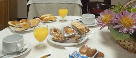 Una mesa de desayuno con pan, bollería, jugo y salsas.