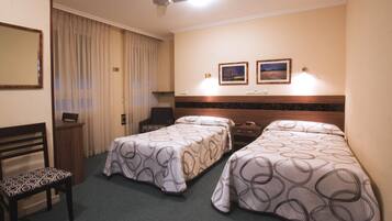 A hotel room with two single beds, a desk, a chair, a ceiling fan, and two framed pictures on the wall.
