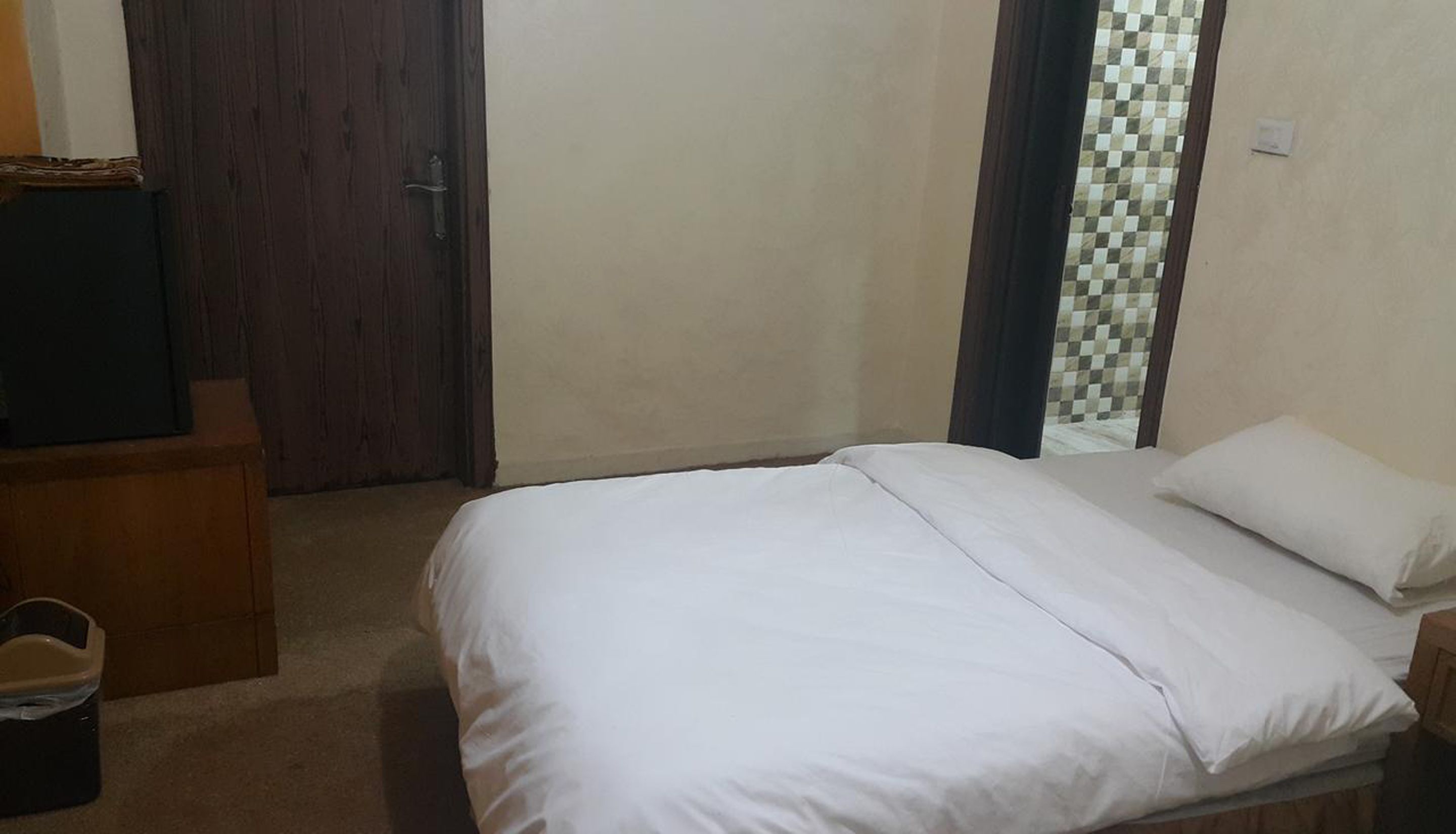 A bedroom with a bed, a wooden dresser, and a door.