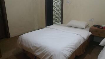 A single bed with white linens in a room with beige walls and a checkered pattern on the wall behind the bed.