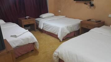 Quarto de hotel com três camas de solteiro, mesas de cabeceira de madeira, uma televisão de tela plana e uma pequena mesa com um controle remoto.