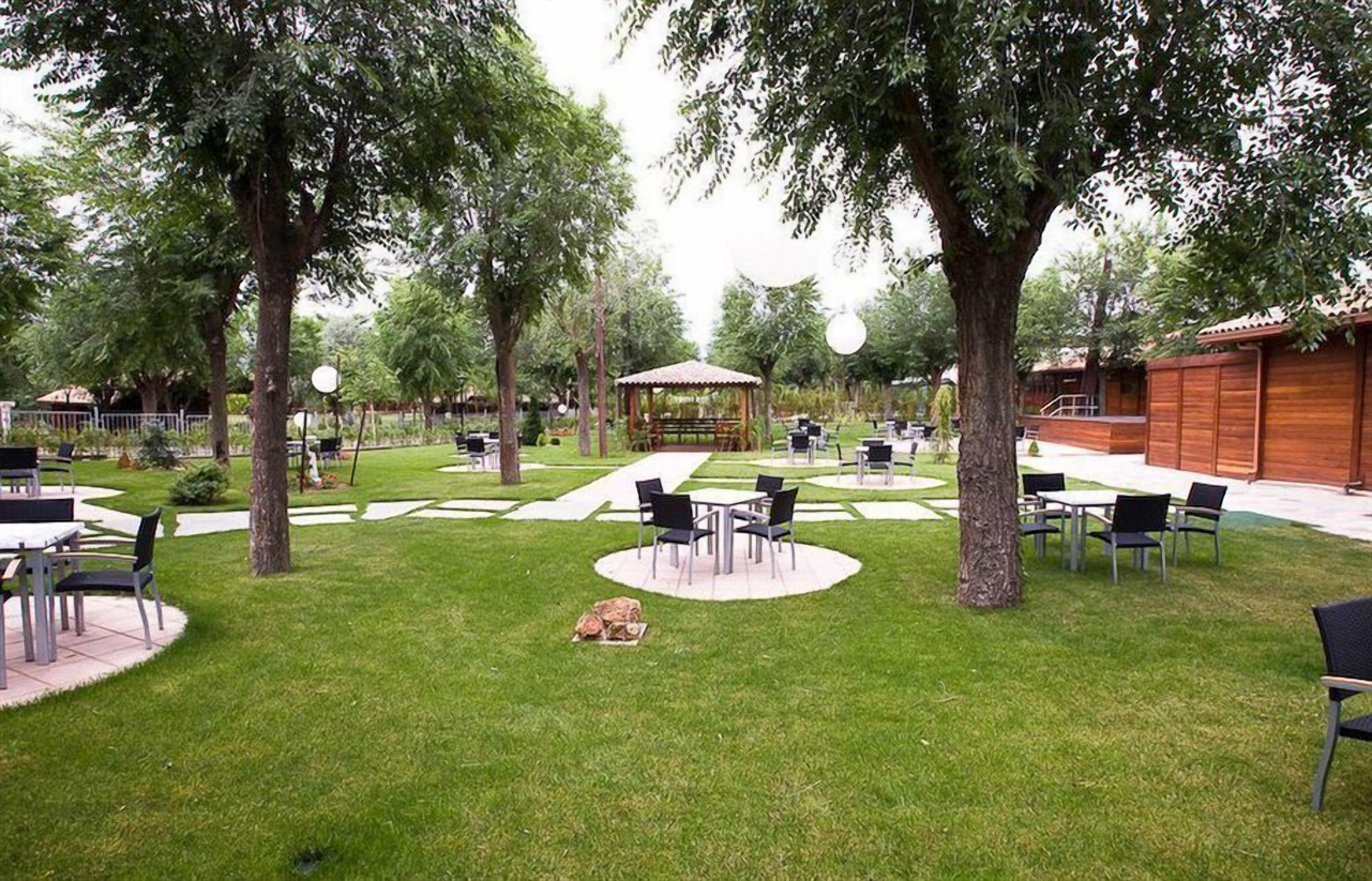 Un área de patio al aire libre con mesas y sillas, rodeada de árboles y un pabellón.